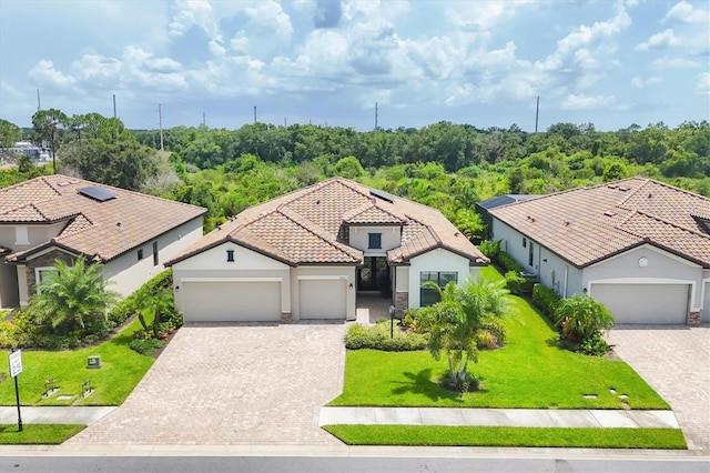 view of front of property featuring decorative driveway, a garage, a tiled roof, a front yard, and stucco siding