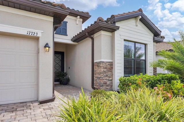doorway to property featuring a tile roof, stone siding, and stucco siding