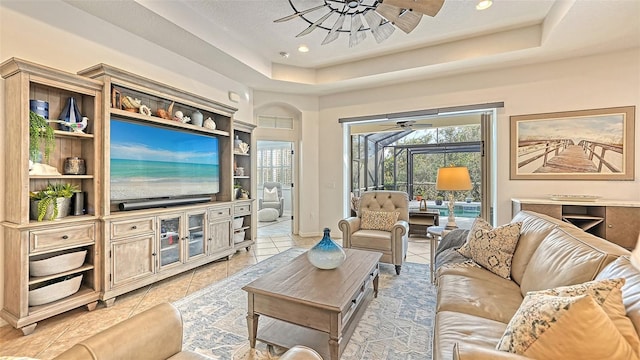 living room featuring a tray ceiling, light tile patterned floors, and ceiling fan