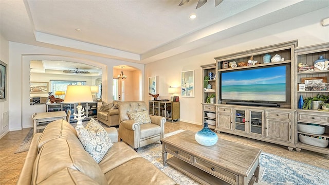 living room with ceiling fan with notable chandelier, a textured ceiling, light tile patterned floors, and a tray ceiling