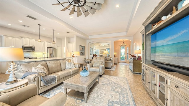 tiled living room with ceiling fan and a tray ceiling