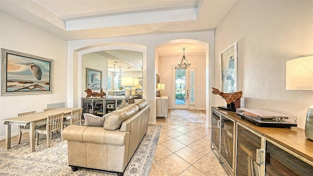 living room with a notable chandelier, light tile patterned flooring, and a tray ceiling