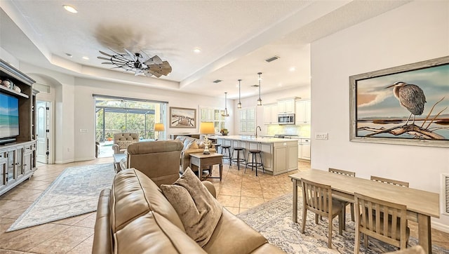 living room featuring a textured ceiling, light tile patterned floors, a raised ceiling, and ceiling fan