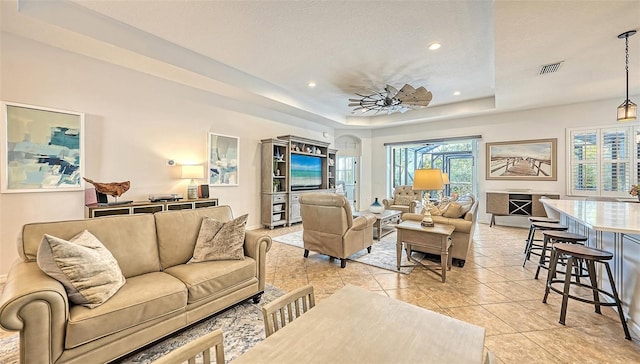 tiled living room with a raised ceiling and ceiling fan