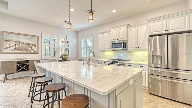 kitchen featuring decorative light fixtures, light tile patterned flooring, stainless steel appliances, sink, and a center island with sink