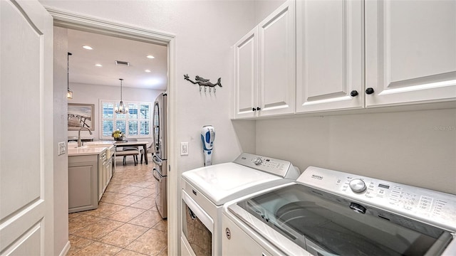 washroom with light tile patterned flooring, sink, an inviting chandelier, washer and dryer, and cabinets