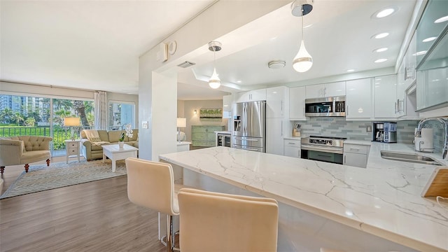 kitchen with a breakfast bar area, white cabinets, stainless steel appliances, hanging light fixtures, and sink