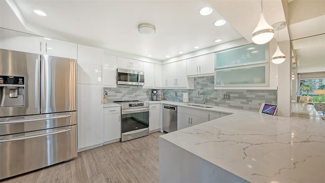 kitchen with stainless steel appliances, decorative backsplash, sink, light stone counters, and light hardwood / wood-style flooring