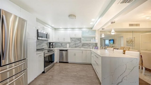 kitchen with decorative backsplash, appliances with stainless steel finishes, kitchen peninsula, and light hardwood / wood-style flooring