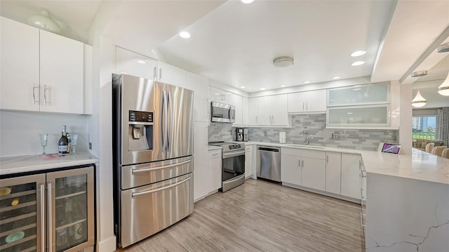 kitchen with appliances with stainless steel finishes, tasteful backsplash, white cabinets, light wood-type flooring, and beverage cooler