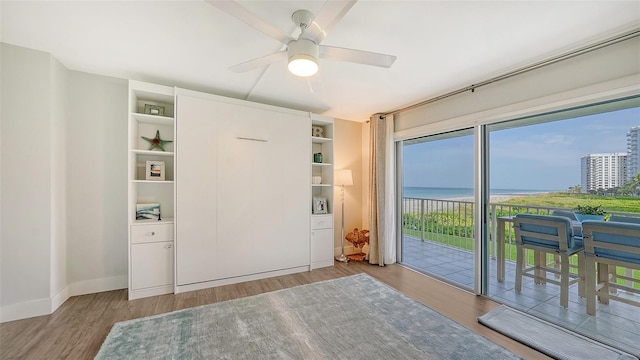 bedroom featuring light hardwood / wood-style floors, a water view, access to exterior, and ceiling fan