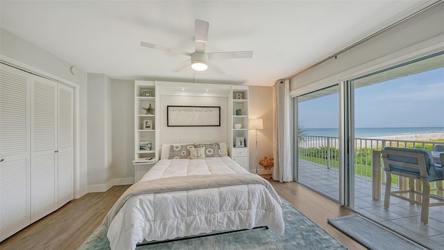 bedroom featuring a water view, access to outside, light wood-type flooring, and ceiling fan