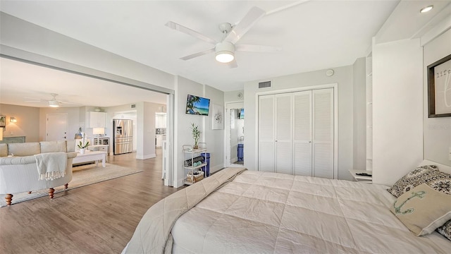 bedroom with stainless steel fridge, a closet, wood-type flooring, and ceiling fan