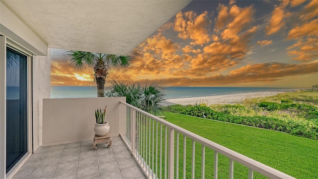 balcony at dusk featuring a water view and a view of the beach