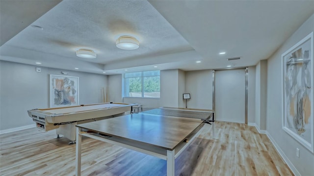 game room with light hardwood / wood-style flooring, a textured ceiling, pool table, a tray ceiling, and elevator