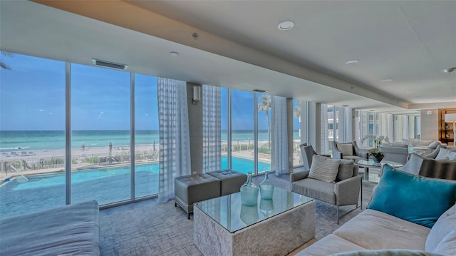 living room with a wall of windows, a water view, and a beach view