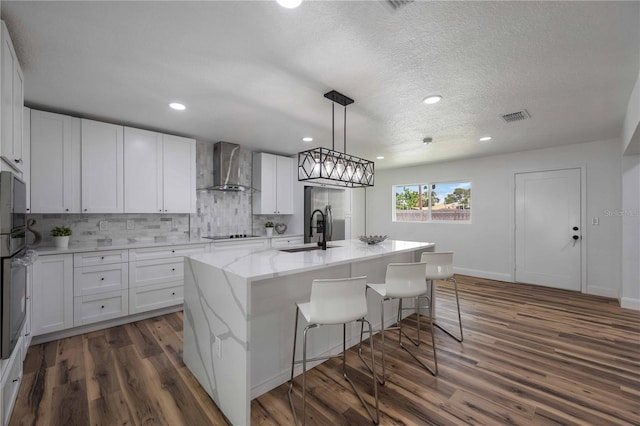 kitchen featuring white cabinetry, dark hardwood / wood-style flooring, wall chimney exhaust hood, sink, and a kitchen island with sink