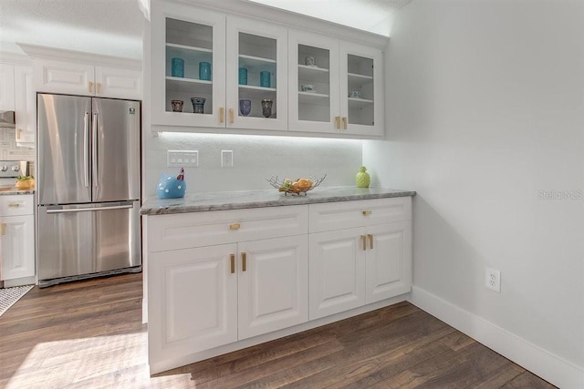 bar featuring light stone counters, dark hardwood / wood-style flooring, stainless steel fridge, and white cabinets