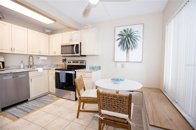 kitchen with ceiling fan, stainless steel appliances, sink, light stone countertops, and light tile patterned floors