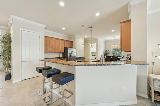 kitchen with stainless steel fridge, dark stone countertops, light tile patterned floors, and kitchen peninsula