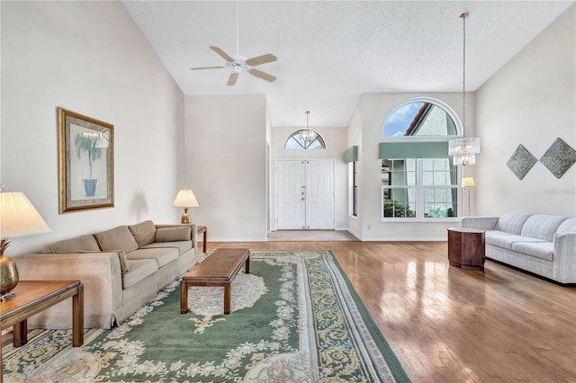 living room featuring hardwood / wood-style flooring, ceiling fan with notable chandelier, high vaulted ceiling, and a textured ceiling