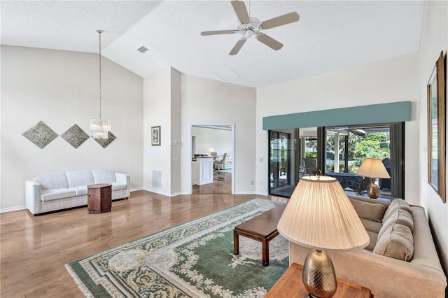 living room with high vaulted ceiling, wood-type flooring, ceiling fan with notable chandelier, and a textured ceiling