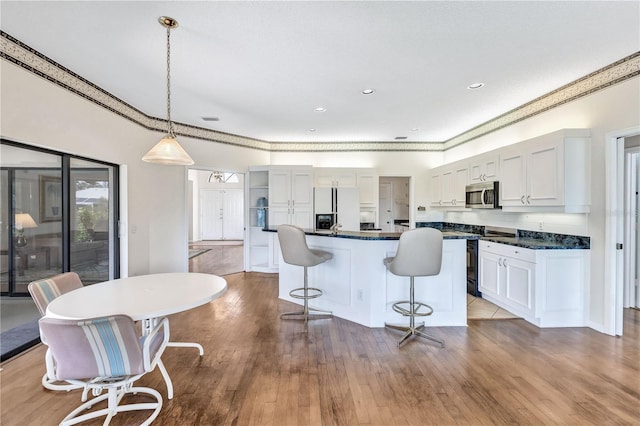 kitchen featuring a breakfast bar area, hanging light fixtures, refrigerator with ice dispenser, a kitchen island, and white cabinets