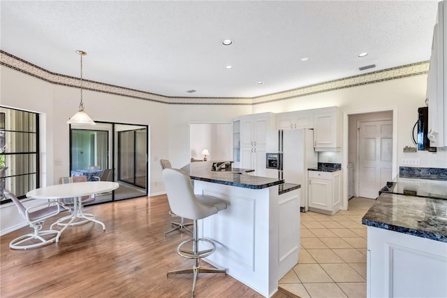 kitchen with sink, white cabinetry, white refrigerator with ice dispenser, a textured ceiling, and decorative light fixtures