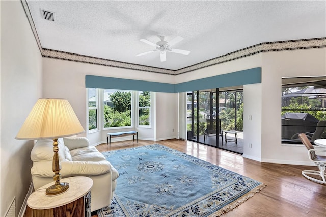 living room with ceiling fan, wood-type flooring, ornamental molding, and a textured ceiling