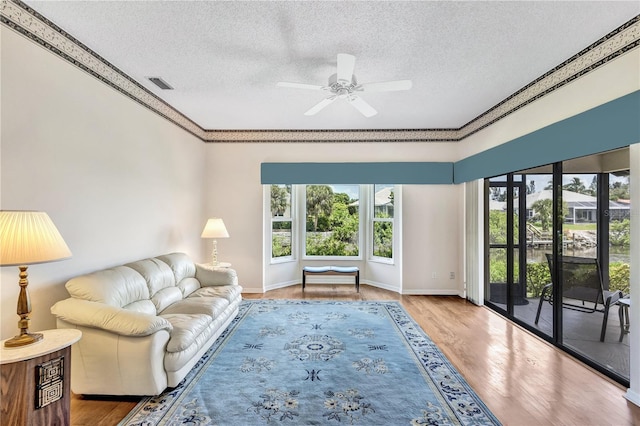 living room featuring ceiling fan, wood-type flooring, a textured ceiling, and ornamental molding