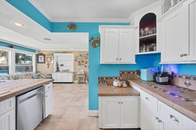 kitchen featuring white cabinets, light tile patterned floors, stainless steel dishwasher, crown molding, and tile counters