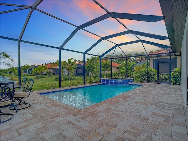 pool at dusk featuring a lawn, a lanai, an in ground hot tub, and a patio