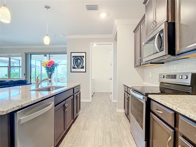 kitchen with crown molding, sink, light stone countertops, appliances with stainless steel finishes, and decorative light fixtures