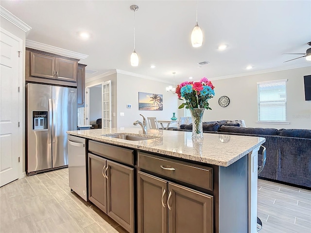 kitchen featuring appliances with stainless steel finishes, dark brown cabinetry, crown molding, sink, and a center island with sink