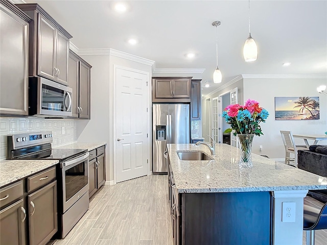 kitchen with sink, stainless steel appliances, hanging light fixtures, and a center island with sink