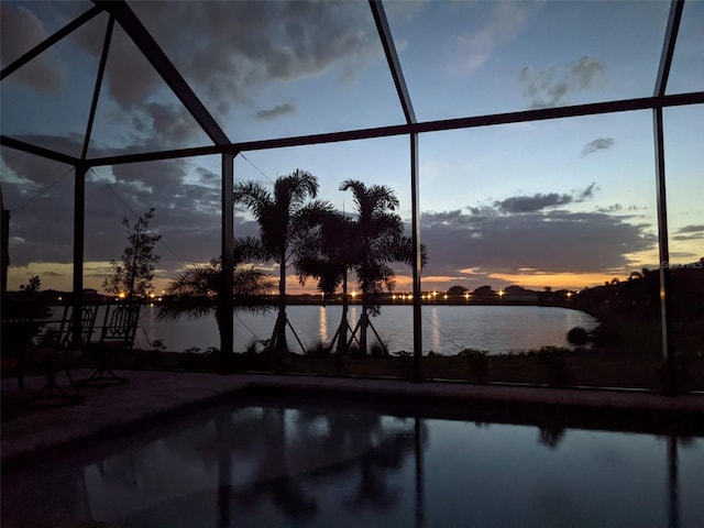 pool at dusk featuring a lanai and a water view