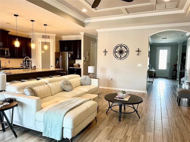 living room with a raised ceiling, light hardwood / wood-style floors, crown molding, sink, and ceiling fan