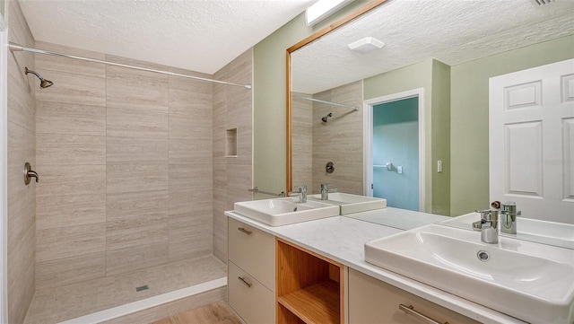 bathroom with a textured ceiling, a tile shower, and vanity