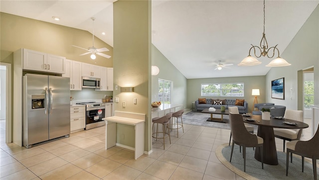 kitchen featuring high vaulted ceiling, ceiling fan with notable chandelier, light tile patterned floors, stainless steel appliances, and white cabinets