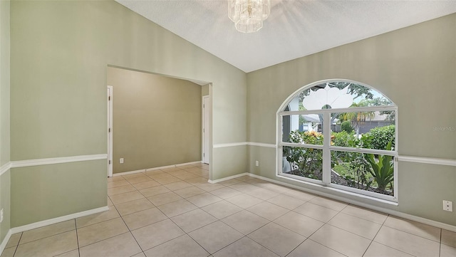 tiled empty room featuring a textured ceiling, vaulted ceiling, and an inviting chandelier