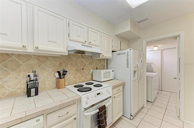 kitchen with light tile patterned floors, tile counters, washer and dryer, white appliances, and under cabinet range hood