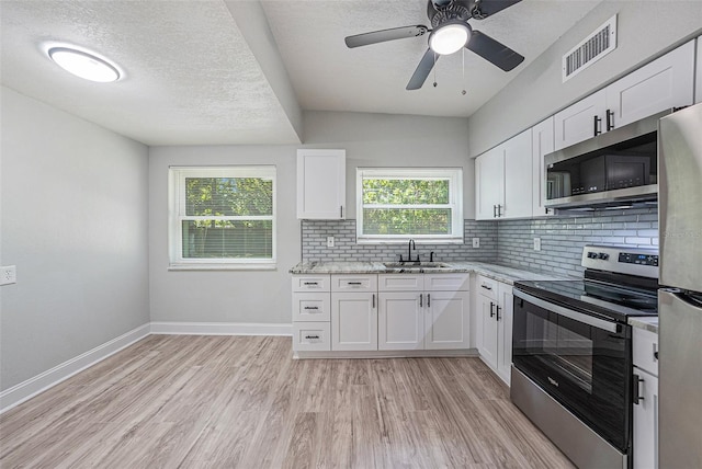 kitchen with white cabinets, light hardwood / wood-style flooring, appliances with stainless steel finishes, sink, and ceiling fan