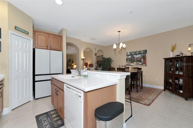 kitchen featuring pendant lighting, light tile patterned floors, white appliances, sink, and a center island with sink