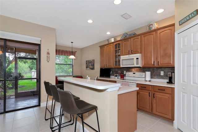 kitchen with a kitchen bar, hanging light fixtures, light tile patterned floors, white appliances, and a kitchen island with sink