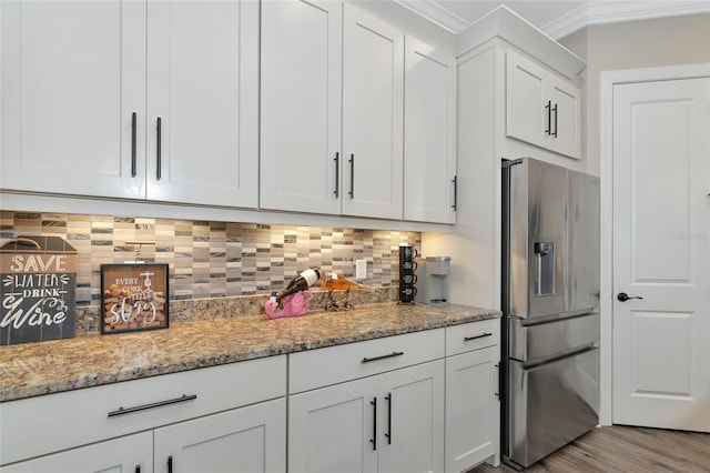 kitchen with hardwood / wood-style floors, stainless steel fridge, light stone counters, white cabinetry, and ornamental molding