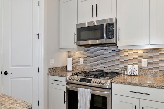 kitchen with white cabinetry, light stone countertops, stainless steel appliances, and backsplash