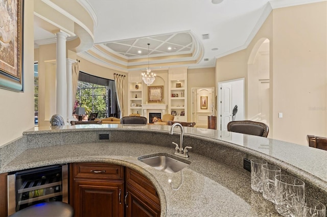 kitchen with ornamental molding, sink, decorative columns, light stone counters, and wine cooler