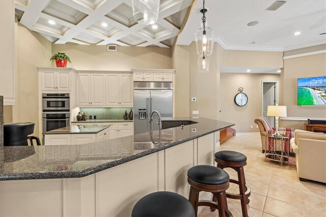 kitchen with appliances with stainless steel finishes, hanging light fixtures, backsplash, light tile patterned flooring, and dark stone countertops