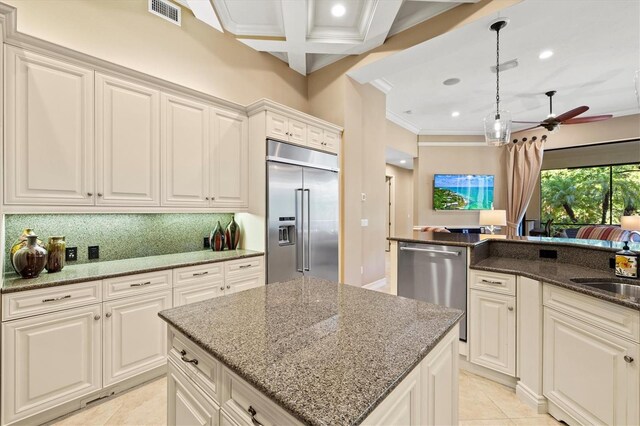 kitchen featuring dark stone counters, a kitchen island, ceiling fan, stainless steel appliances, and ornamental molding