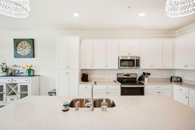 kitchen with light stone counters, crown molding, appliances with stainless steel finishes, white cabinetry, and a sink